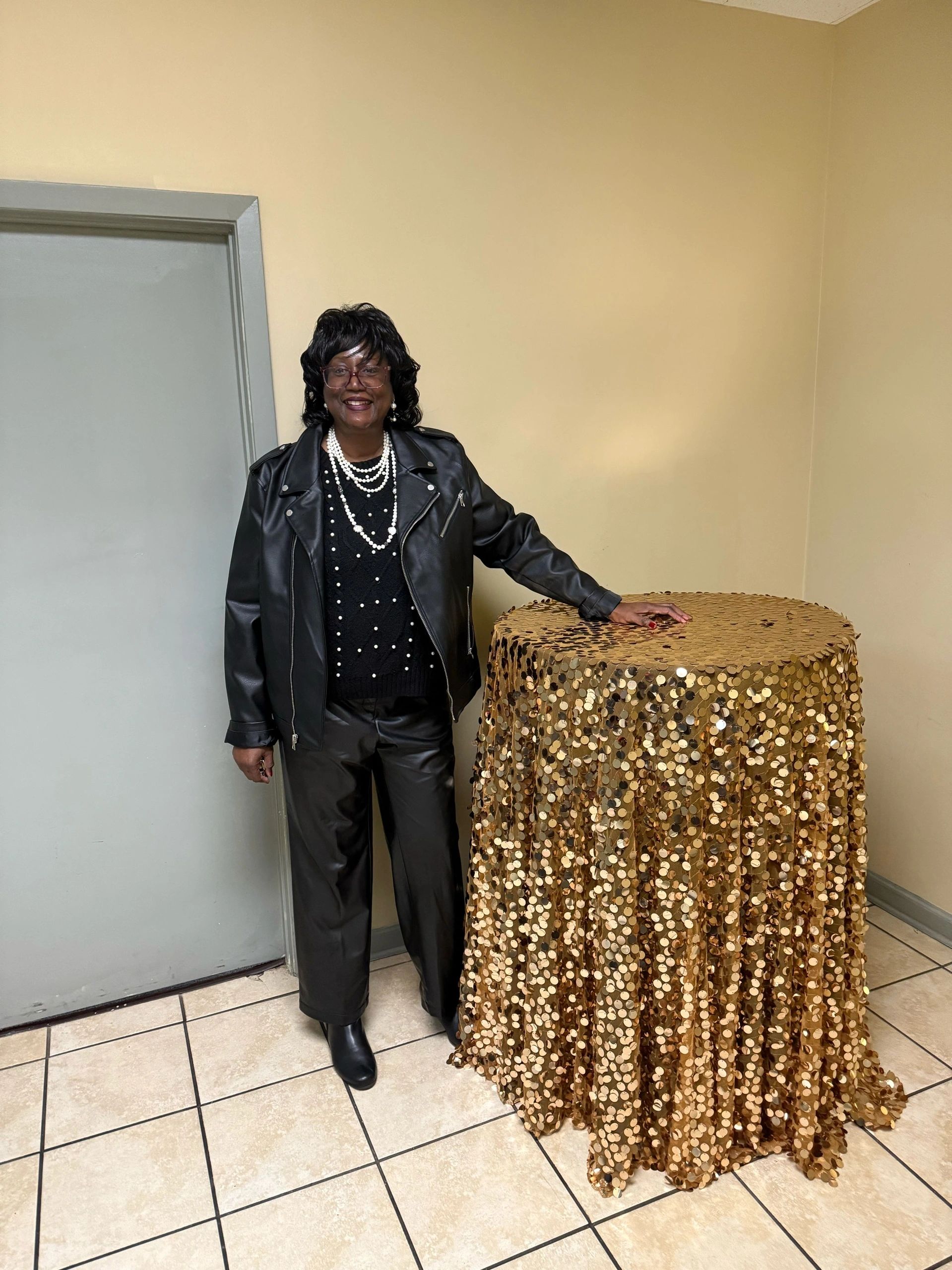 Studio portrait of Dr. Sandra D. Little in a black jacket beside a gold sequin table.